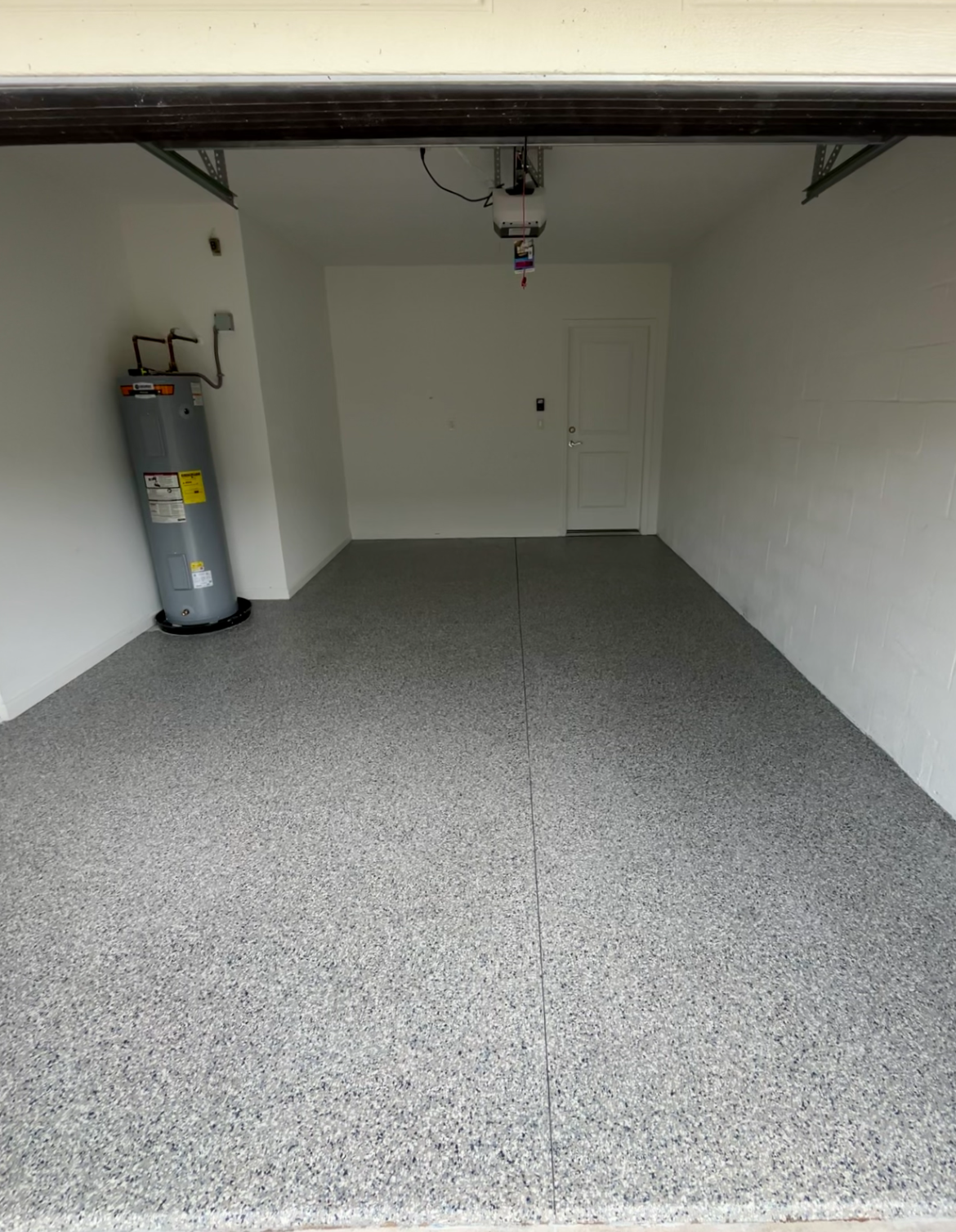 Finished garage with a decorative flake epoxy floor, looking toward the interior wall, water heater, and side door